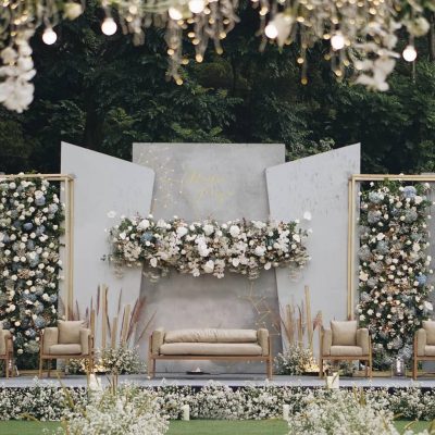 Elegant outdoor wedding stage decorated with white flowers, chandeliers, and modern panel backdrops.