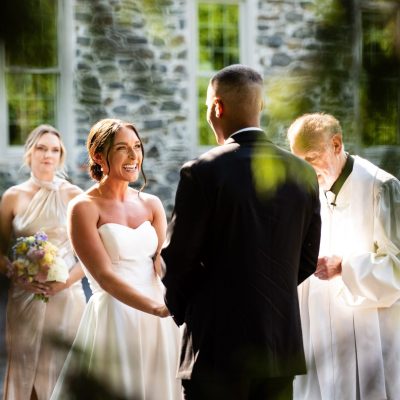 Bride and groom exchanging vows during a wedding ceremony, with bridesmaids and officiant standing nearby.