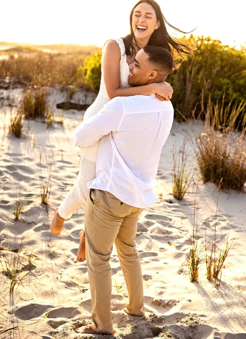 Romantic engagement photography capturing a man lifting a woman in a joyful beach moment during golden hour.