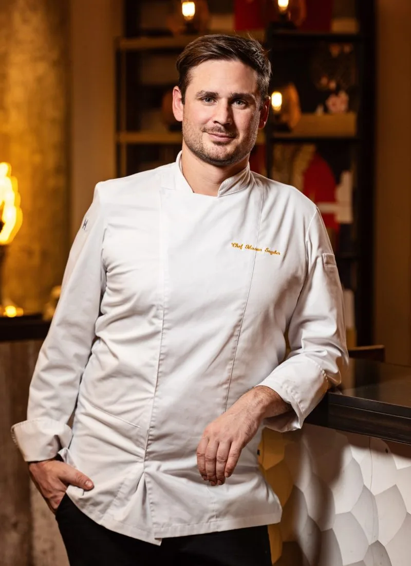 A professional chef confidently posing in a refined restaurant setting, showcasing personality and professionalism — a strong example of corporate photography for culinary branding.