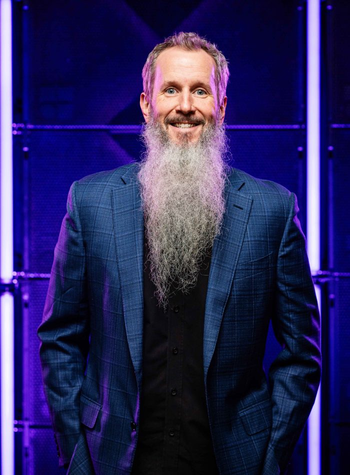 Professional headshot featuring executive in formal business attire against modern purple backdrop